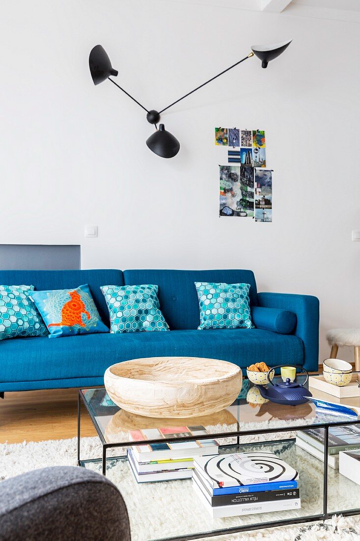 Designerlampe an der Wand über blauem Sofa, filigraner Couchtisch