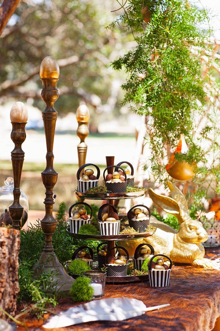 Oster-Cupcakes auf Tisch im Wald dekoriert mit Hasenfigur und Ostereiern auf Kerzensständern