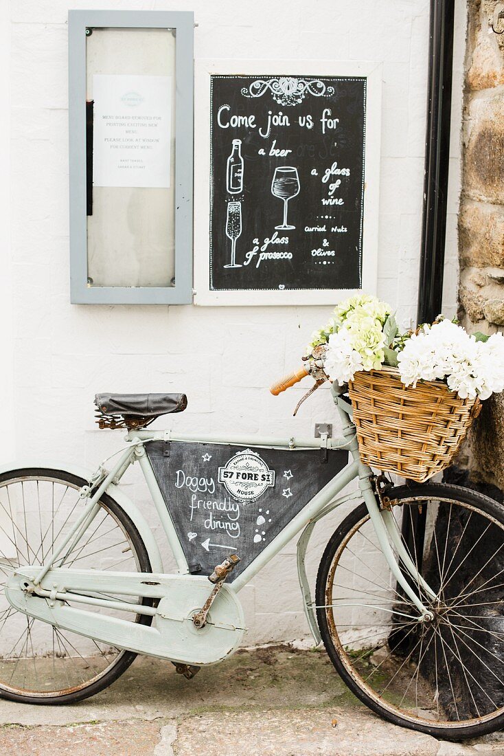 Fahrrad mit Korb voller Blumen und Werbeschild für Restaurant