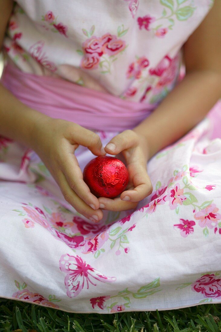 Mädchen im Kleid hält rotes Schokoladenosterei in den Händen