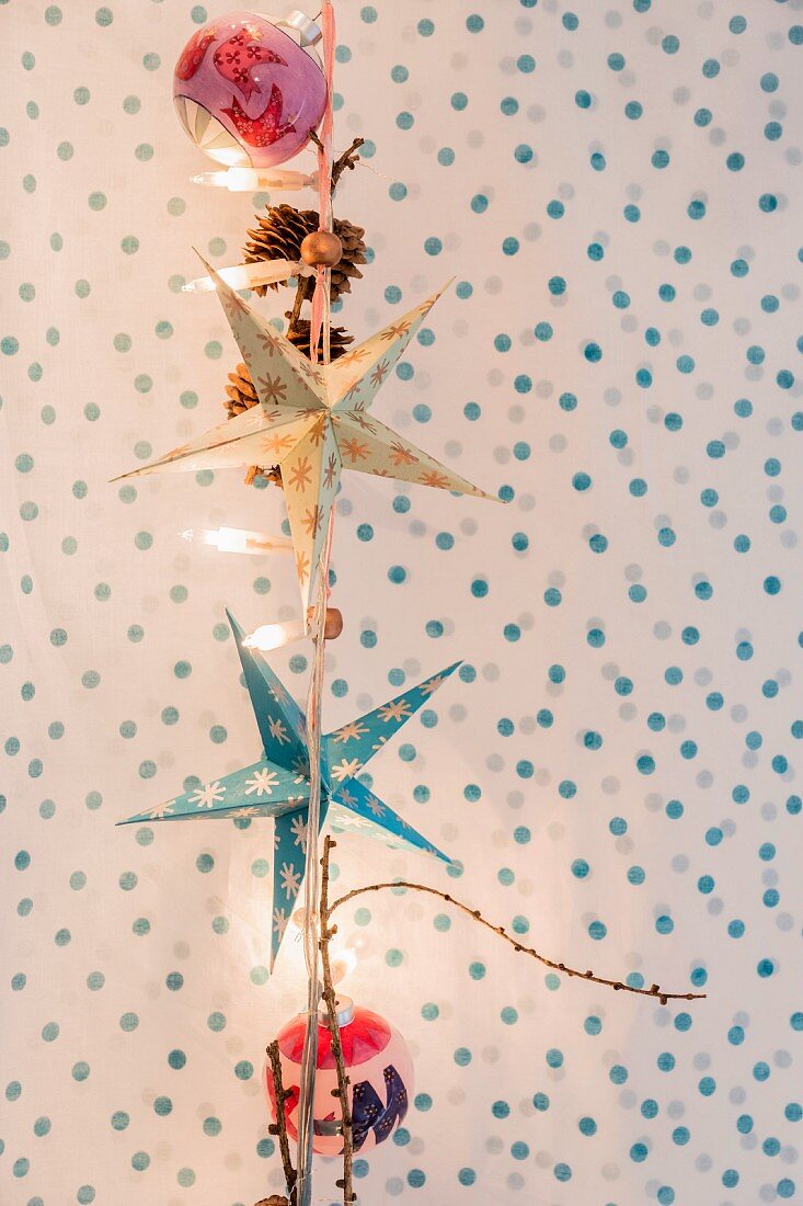 Paper stars and Christmas baubles hanging from fairy lights against polka-dot background