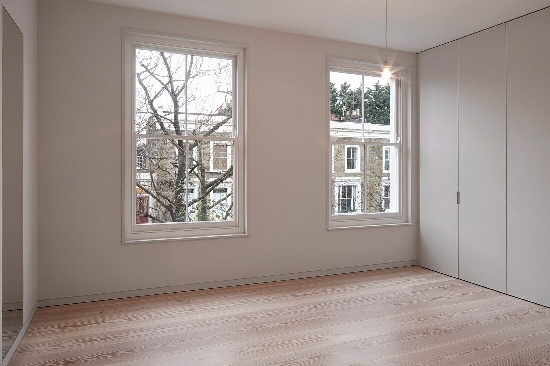 Corner of elegant room with minimalist, floor-to-ceiling fitted cupboards and parquet floor
