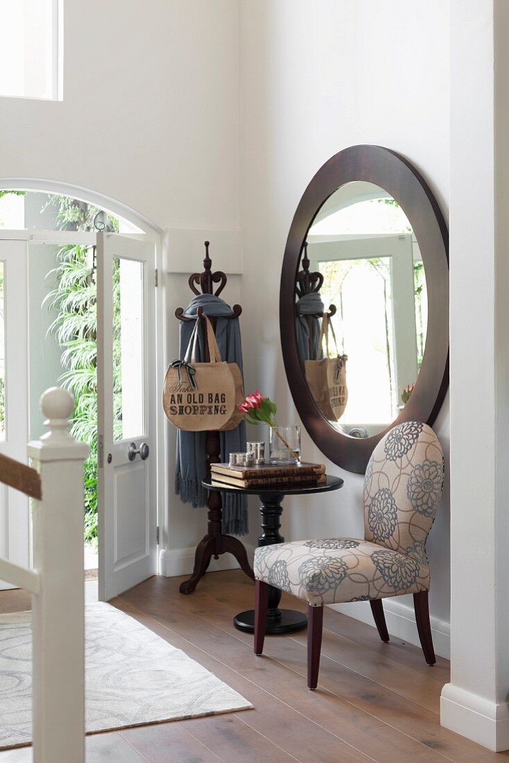 Upholstered chair and bistro table below large round mirror on foyer wall