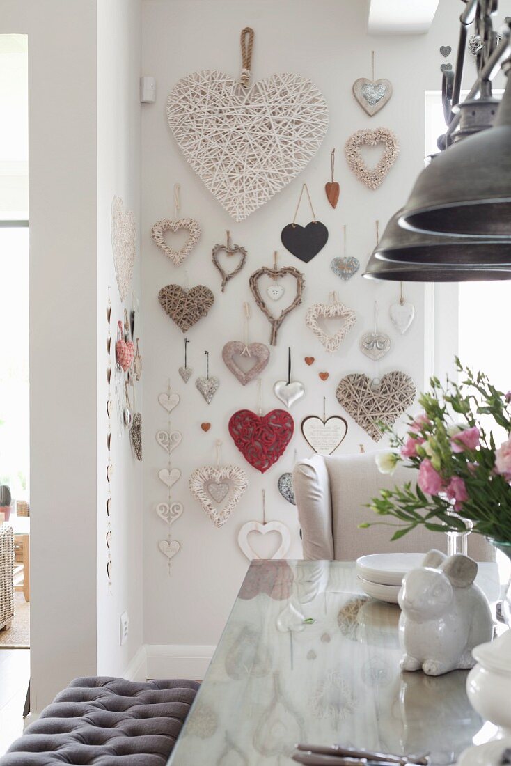 Tisch mit weisser Porzellan Hasenfigur und Frühlingsstrauss, im Hintergrund an Wand Herzformen aus unterschiedlichen Materialien