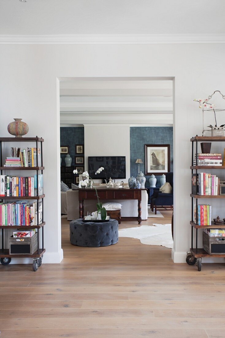 View through wide, open doorway into living room with grey pouffe on continuous wooden floor