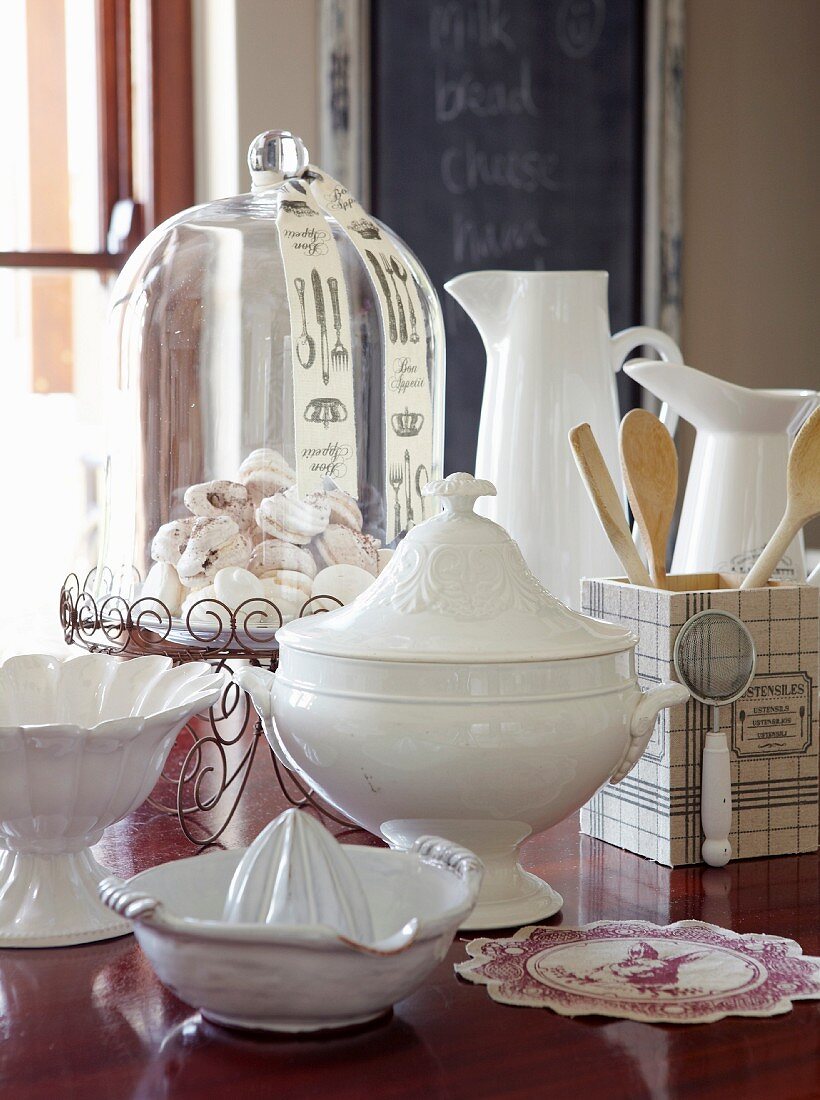 White tureen with lid, citrus squeezer, bowl, pastries under glass cover and jugs