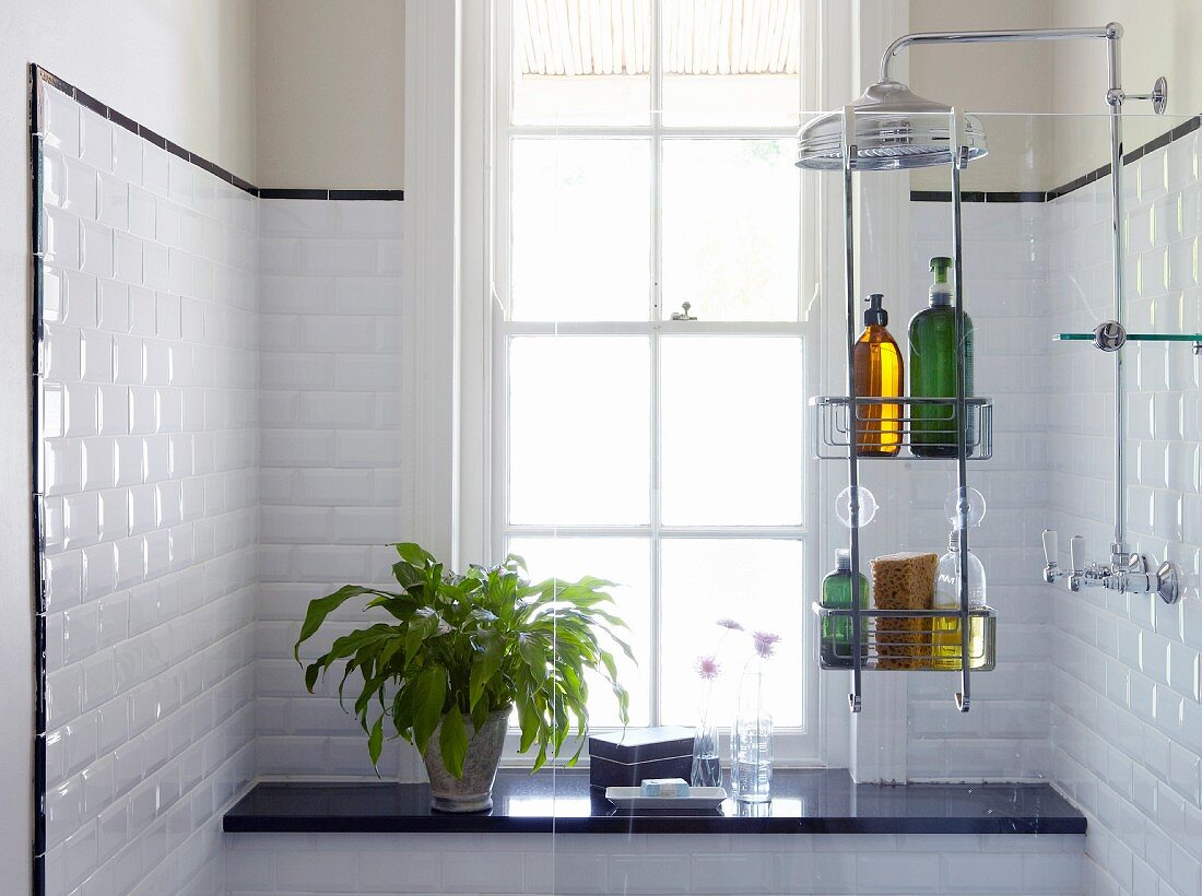 Shelves of toiletries hung on glass partition, black stone shelf below lattice window and white-tiled walls