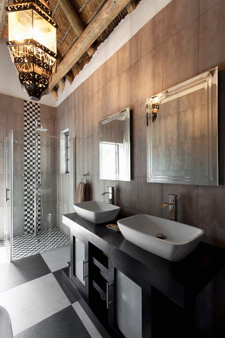 Elegant bathroom with chequered floor, washstand with twin sinks against grey-tiled wall and floor-level shower in background