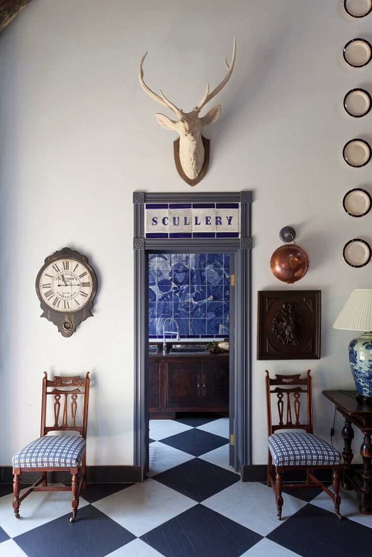 Antike Stühle mit blau-weißen Sitzpolstern neben offener Tür, Blick auf Küchenzeile mit blauer Fliesenwand im Vintage Ambiente