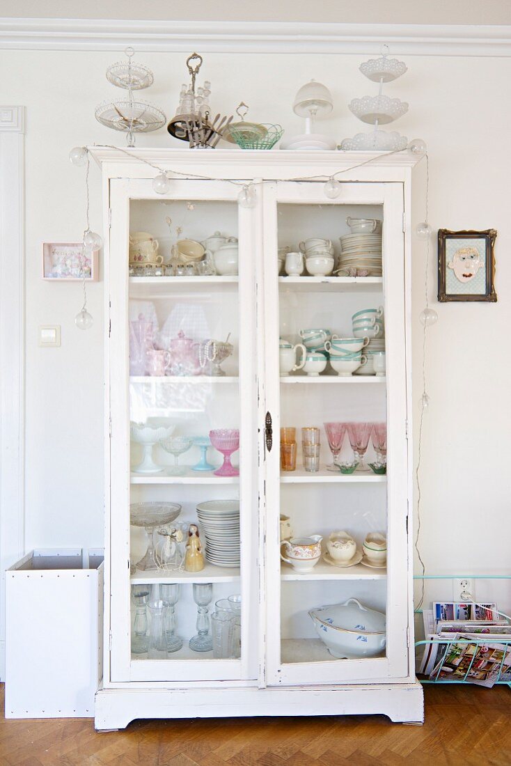 Crockery and glasses in white, shabby-chic, glass-fronted cabinet