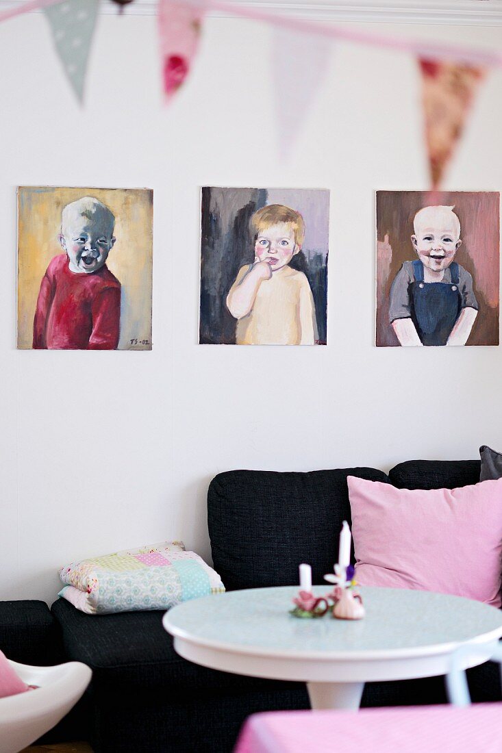 Portrait paintings of children above black sofa with pink scatter cushion and white table