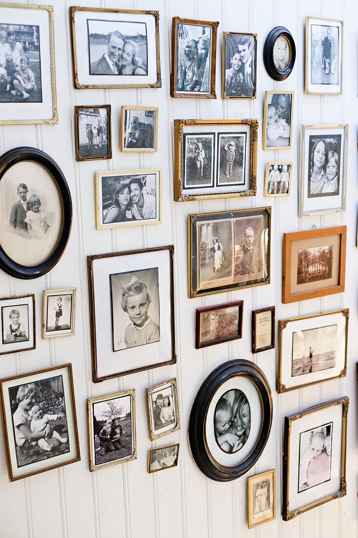 Sammlung von Familienfotos in verschiedenen Rahmen an weisser Holzwand mit nostalgischem Flair