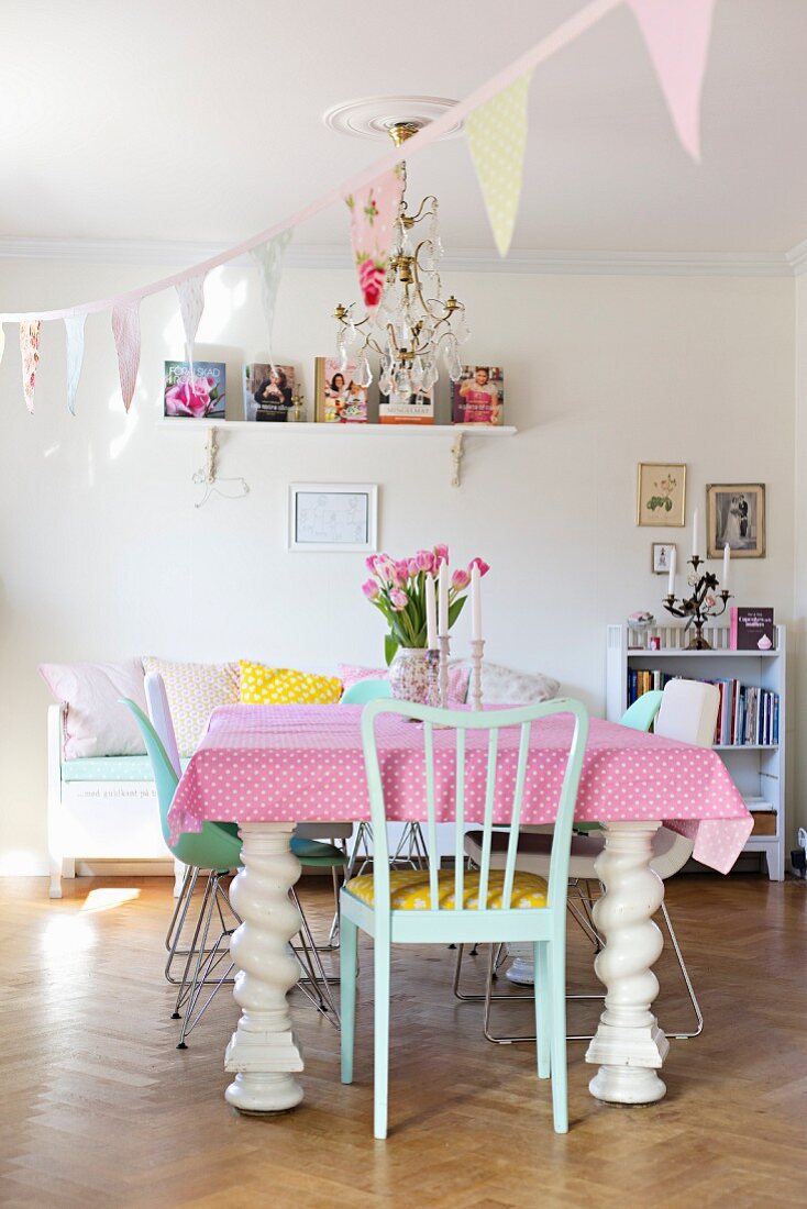 Chunky, white dining table with turned legs and pink and white polka-dot tablecloth in dining room decorated with pastel bunting