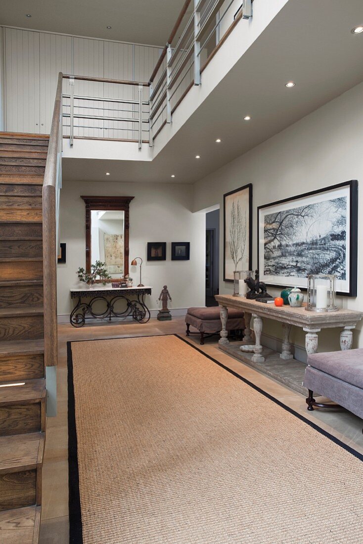 Bright, spacious hallway with antique stone table, black-framed pictures, staircase with wooden treads and metal gallery balustrade