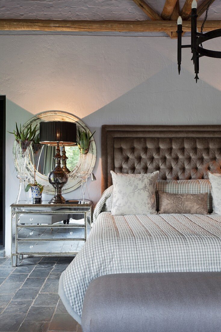 Doppelbett mit gepolstertem Kopfteil und Nachtschränkchen mit Tischleuchte vor rundem Wandspiegel im eleganten Vintage Schlafzimmer