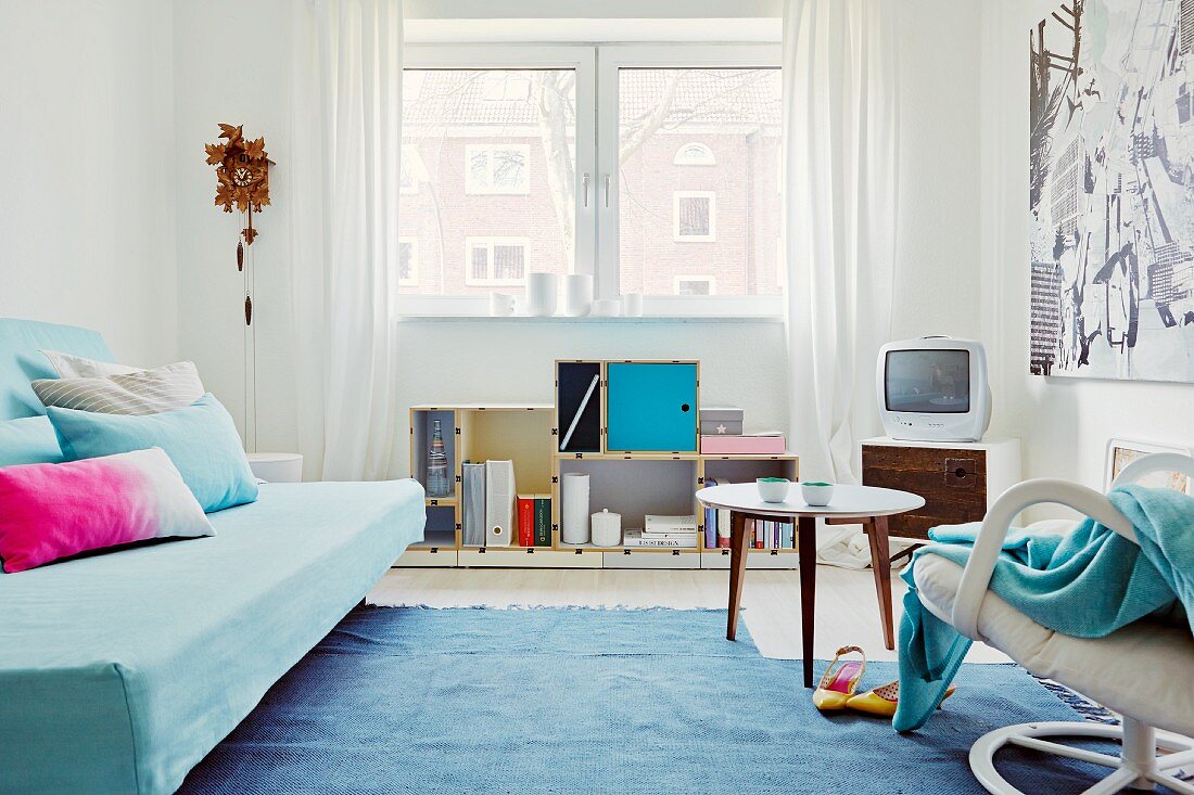 Jugendlicher Wohnraum in Blautönen mit Dekokissen auf Schlafsofa, Kuckucksuhr und leichten Designermöbeln