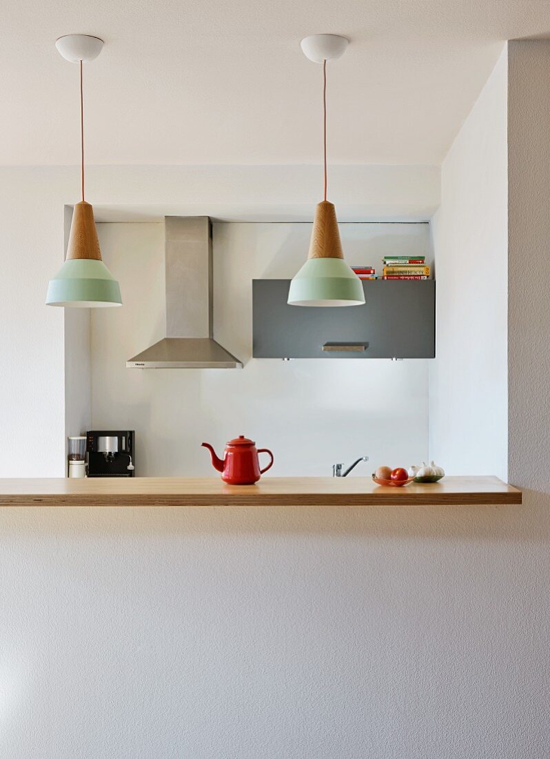 Kitchen counter with wooden worksurface below row of pendant lamps in open-plan, minimalist kitchen