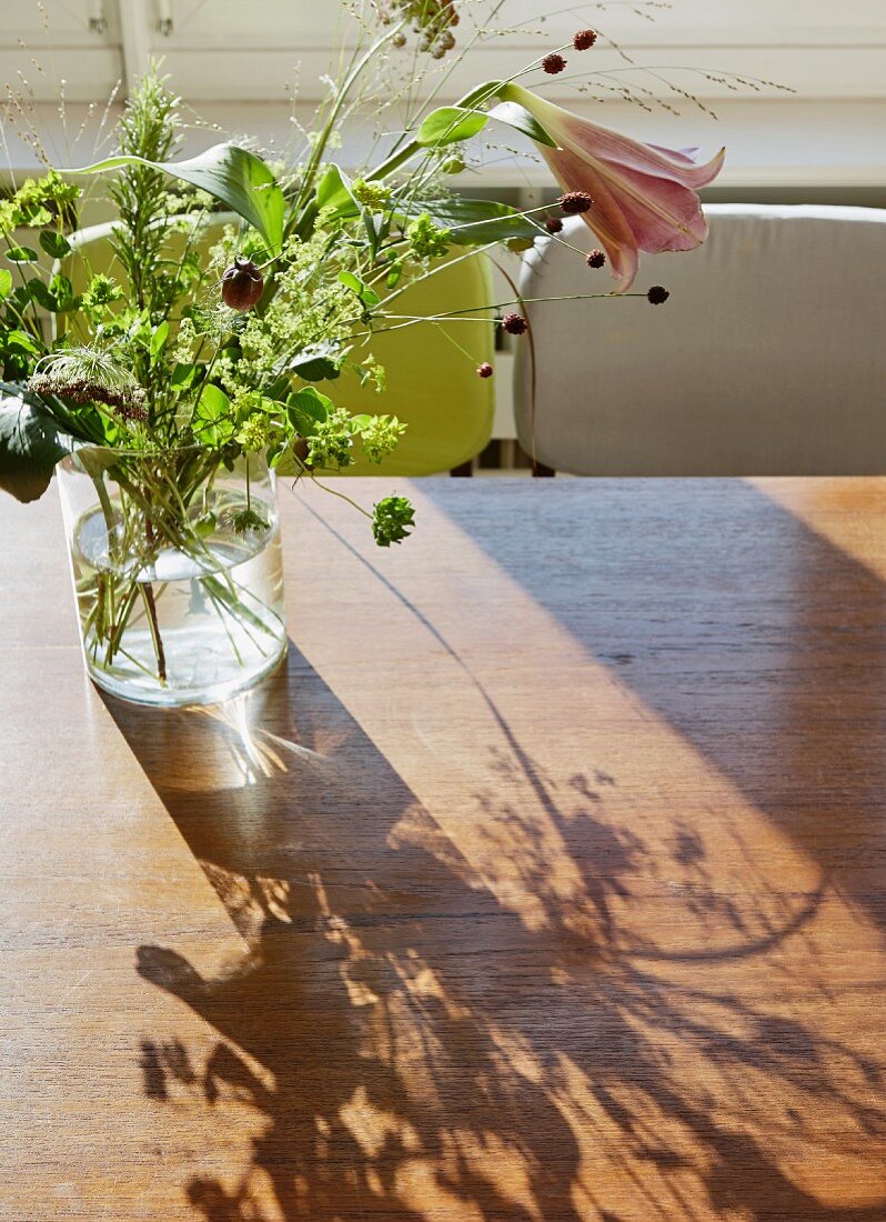 Glass vase of flowers with lily on wooden table; pattern of light and shade