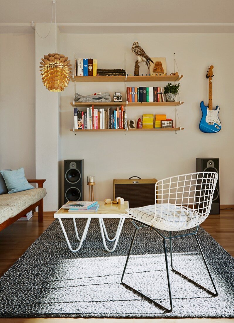 Classic wire chair and coffee table on rug in front of shelf and guitar hung on wall