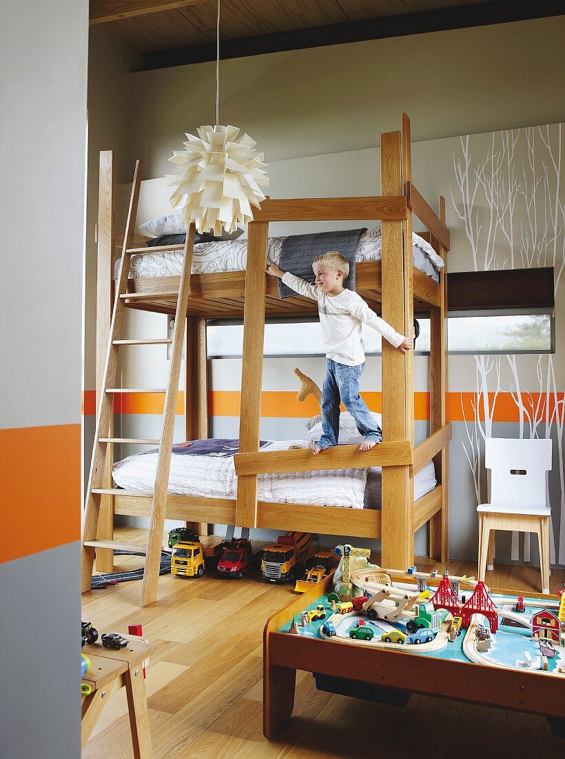 Boy climbing on bunk beds; orange dado stripe and branch structures painted on walls