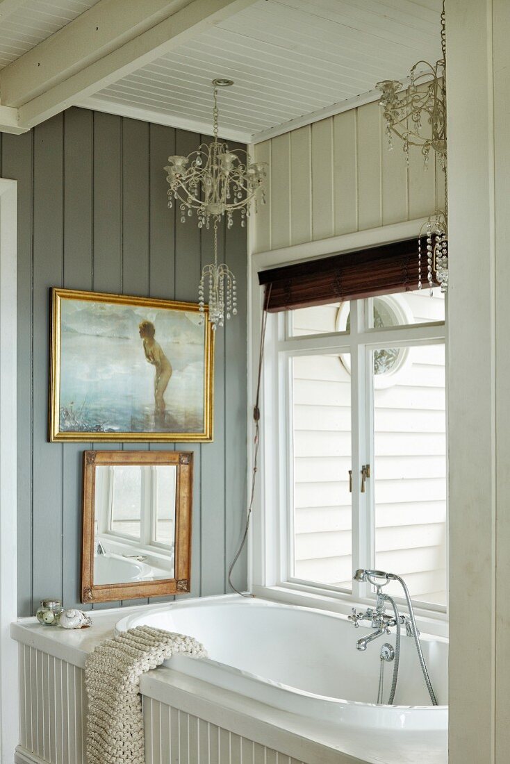 Wood-panelled bathroom with chandeliers above built-in bathtub and gilt-framed pictures on wall