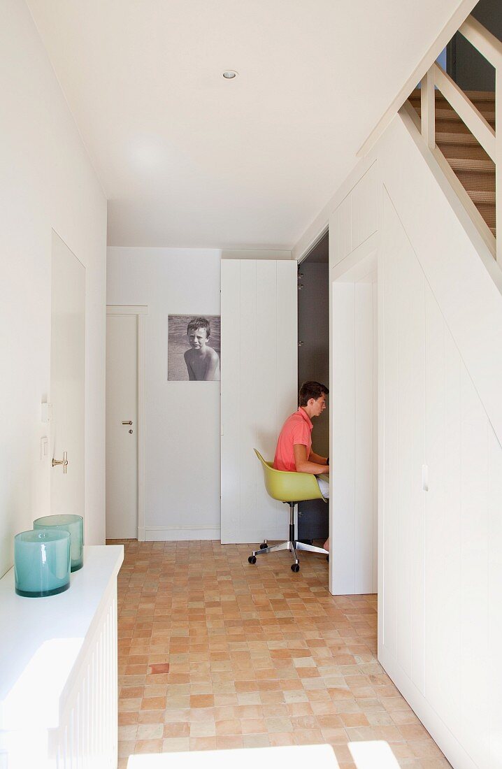 Hallway with integrated home office behind doors below staircase; boy sitting on yellow, classic, designer swivel chair