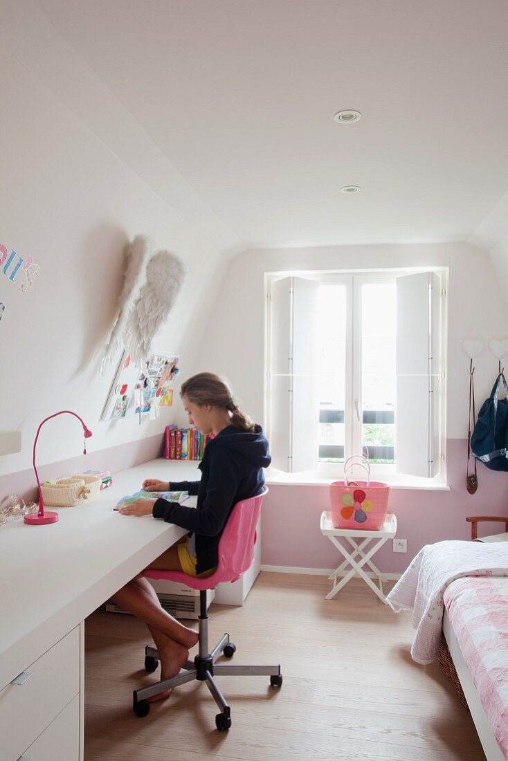 Dachzimmer mit Mädchen auf pinkfarbenem Drehstuhl an seitlich durchlaufender Schreibtischplatte