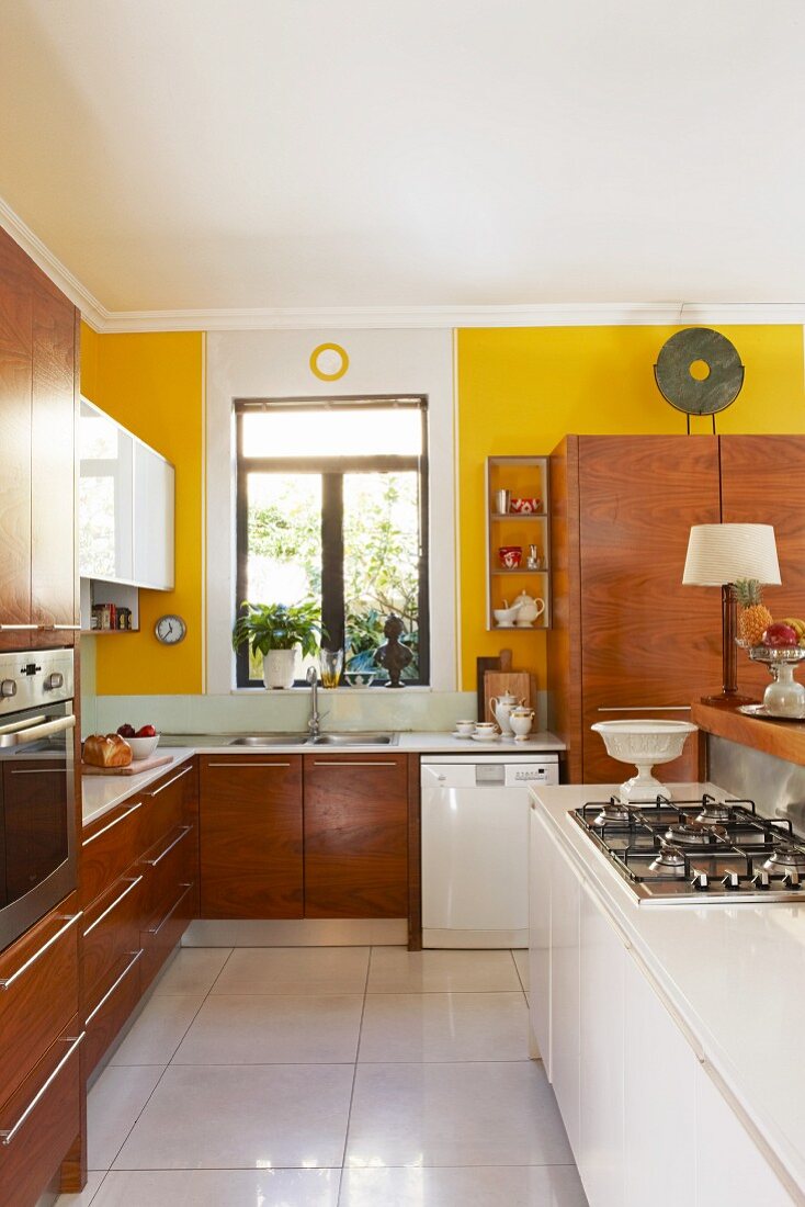 Offene Küche mit weisser Kochinsel und Einbauschränke aus Holz vor gelb getönter Wand