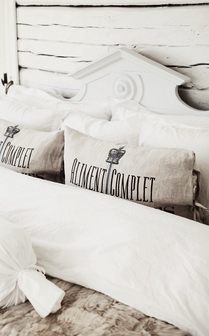 Ausschnitt eines Bettes mit Nackenrollen und Kissen, vor geschnitztem Kopfteil aus Holz in Weiß