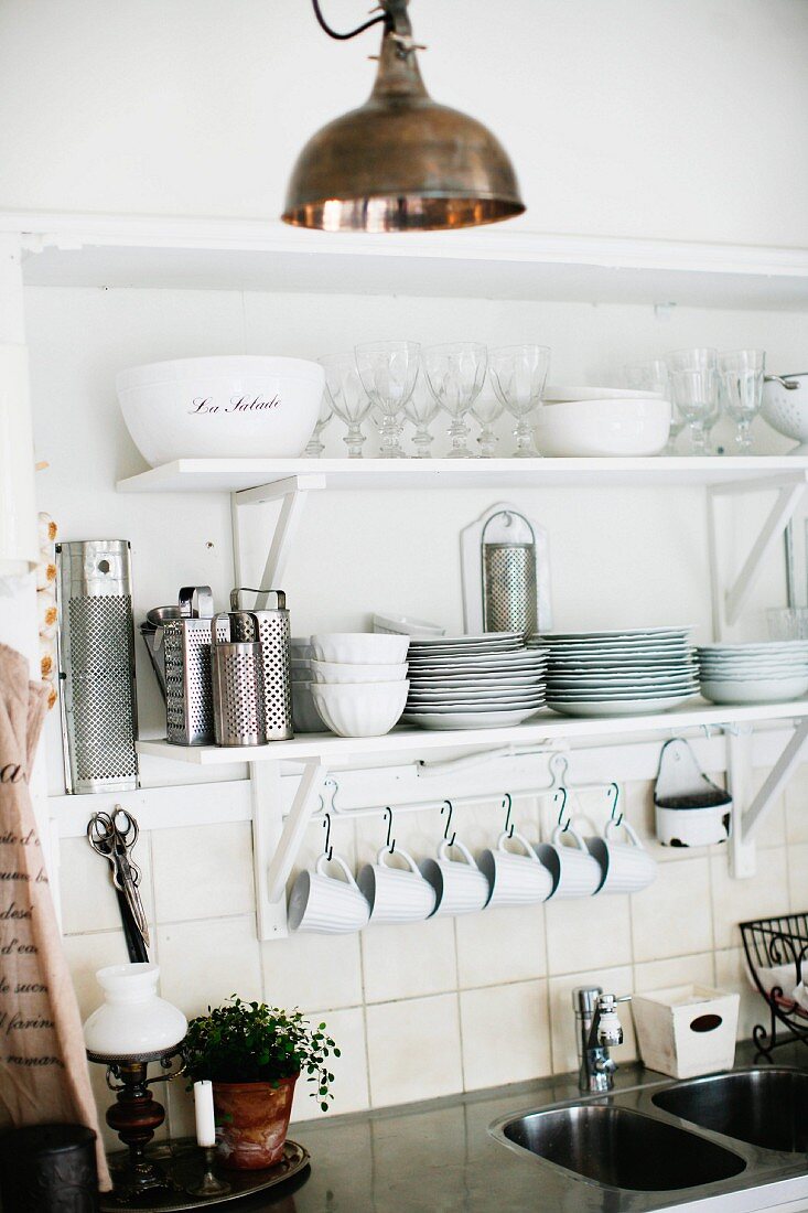 Geschirr und Gläser auf weißem Regalkonsolen, darunter an Wandhakenleiste aufgehängte Tassen