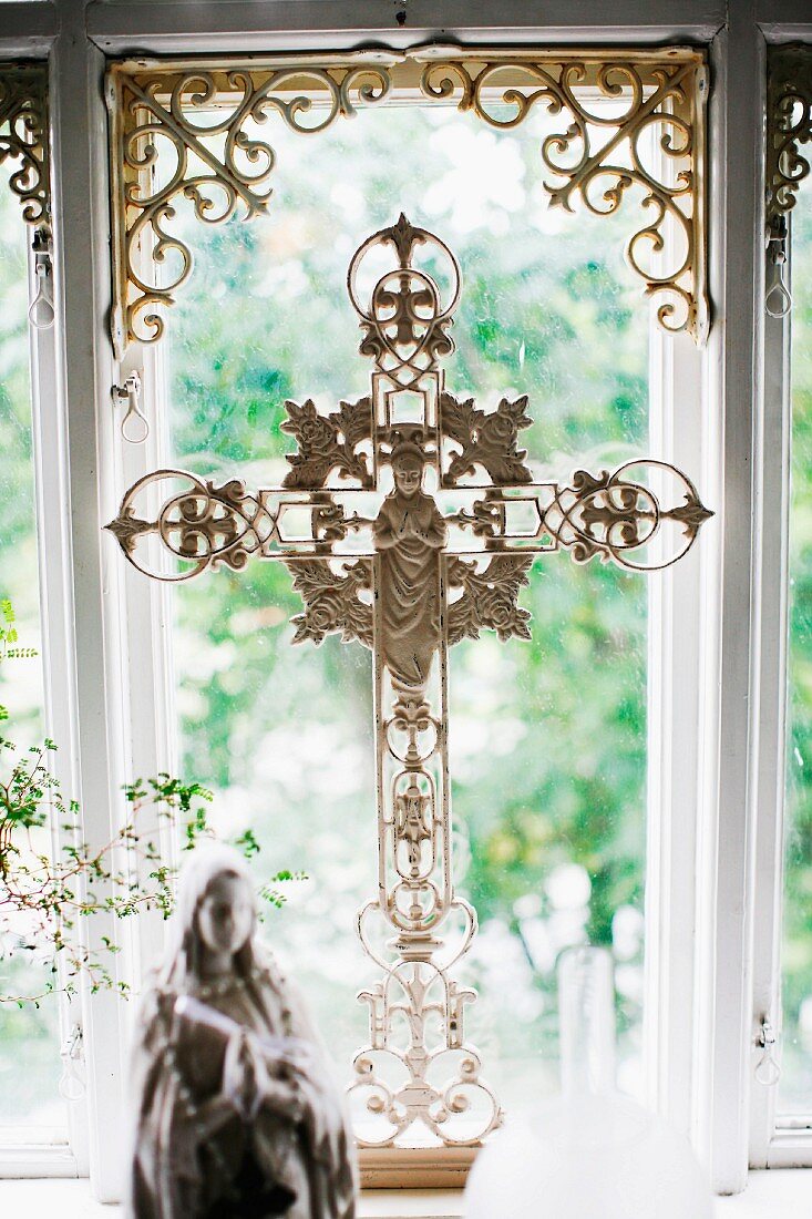 Kreuz mit Figur aus verziertem, weiss lackiertem Metall, vor Fenster