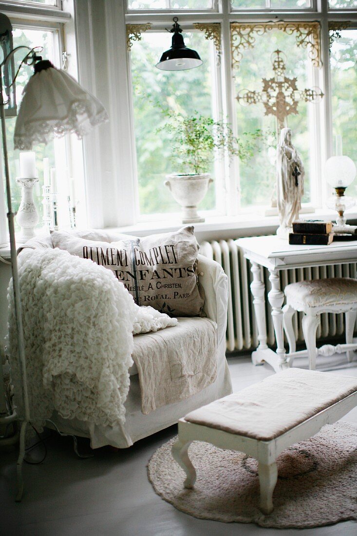 Gemütlicher Sessel mit Kissen und gepolsterter Fussschemel in Erkerbereich vor Fenster