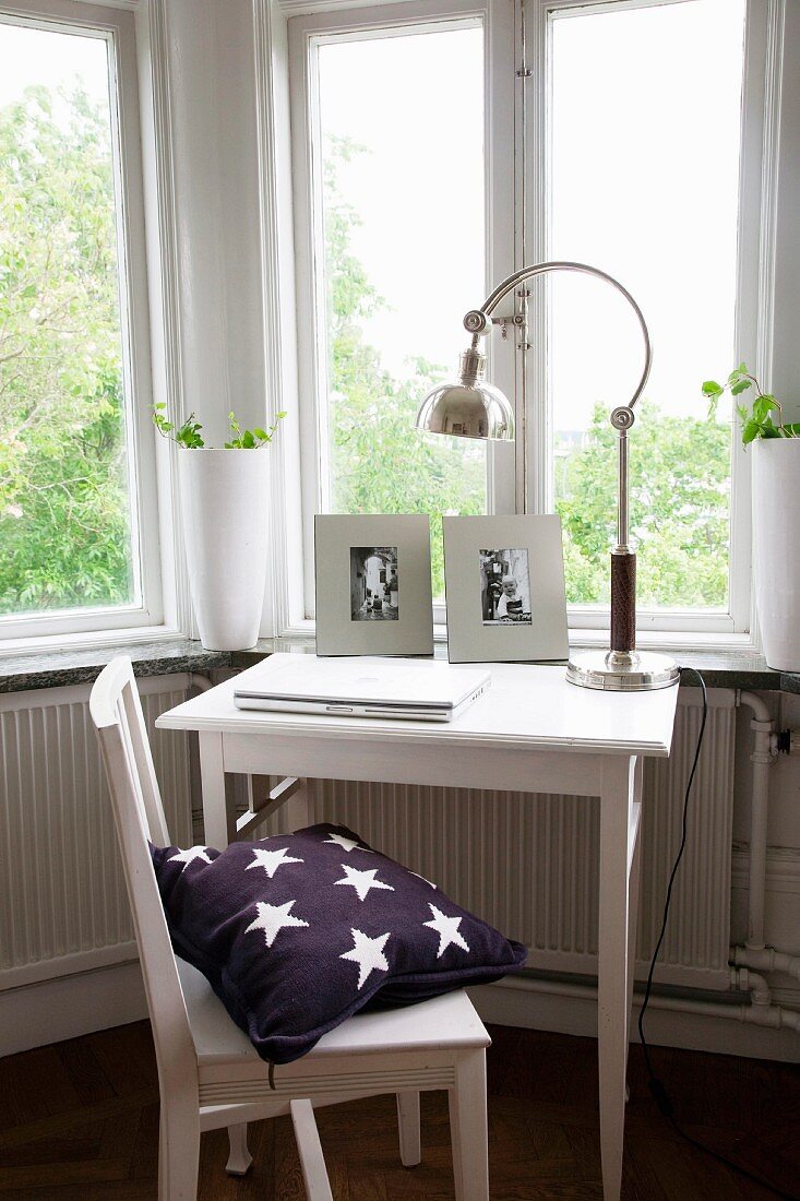 Small work area below window with white-painted chair and table and retro table lamp