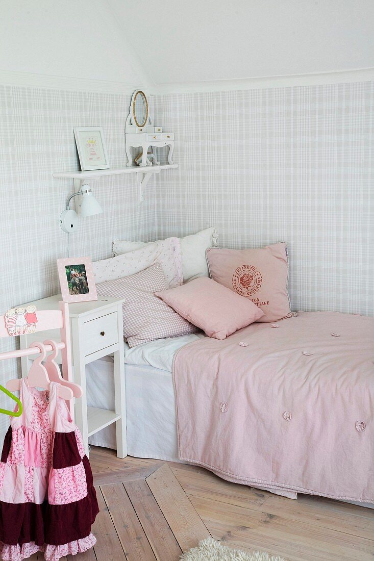 Nostalgisches Mädchenzimmer, Einzelbett mit rosa Bettwäsche in Zimmerecke, an Wand Tapete mit pastellfarbenem Karo Look