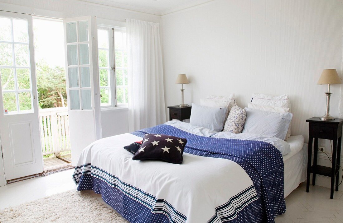 Doppelbett mit blau-weiss gemusterter Tagesdecke, seitlich Nachtkästchen aus dunklem Holz im Schlafzimmer