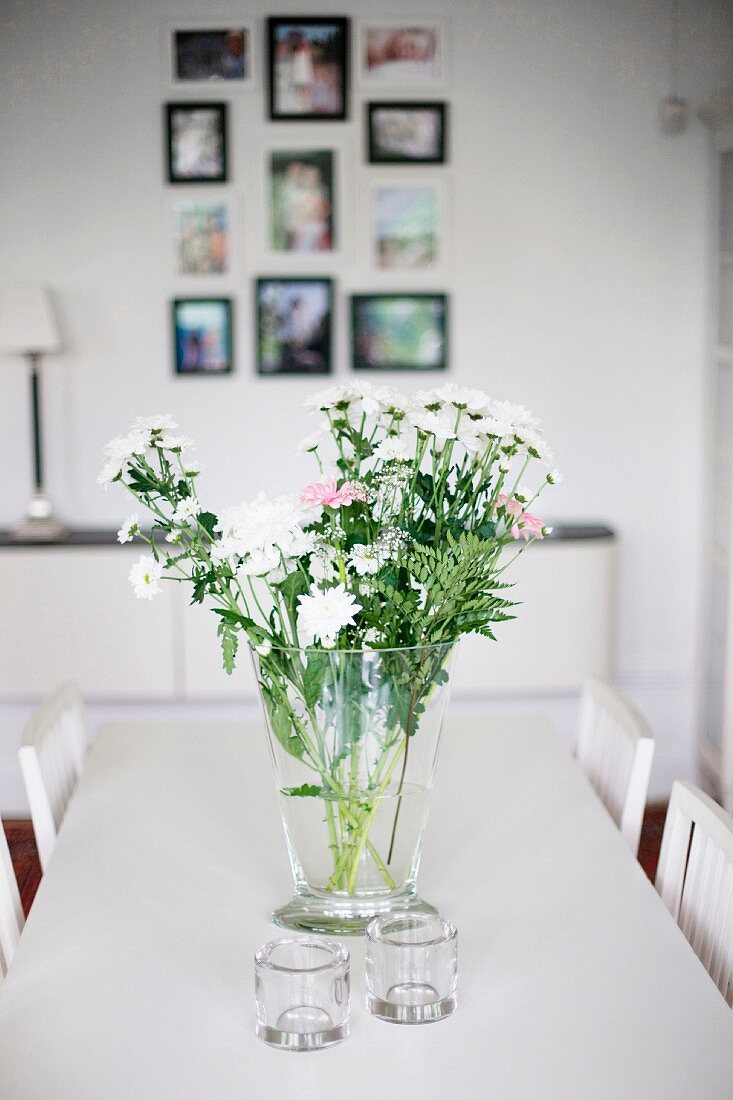 Blumenstrauss in Glasvase und Windlichter auf weißem Esstisch
