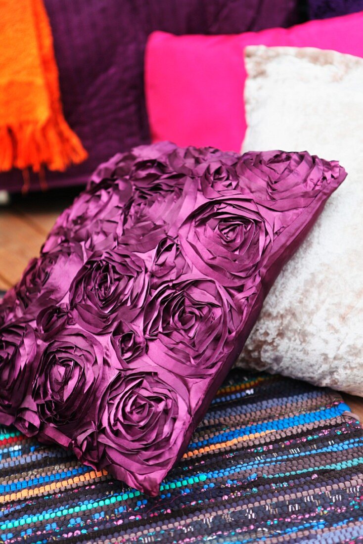 Kissen mit violettem Bezug in Seidenoptik und Rosenmuster auf Flickenteppich