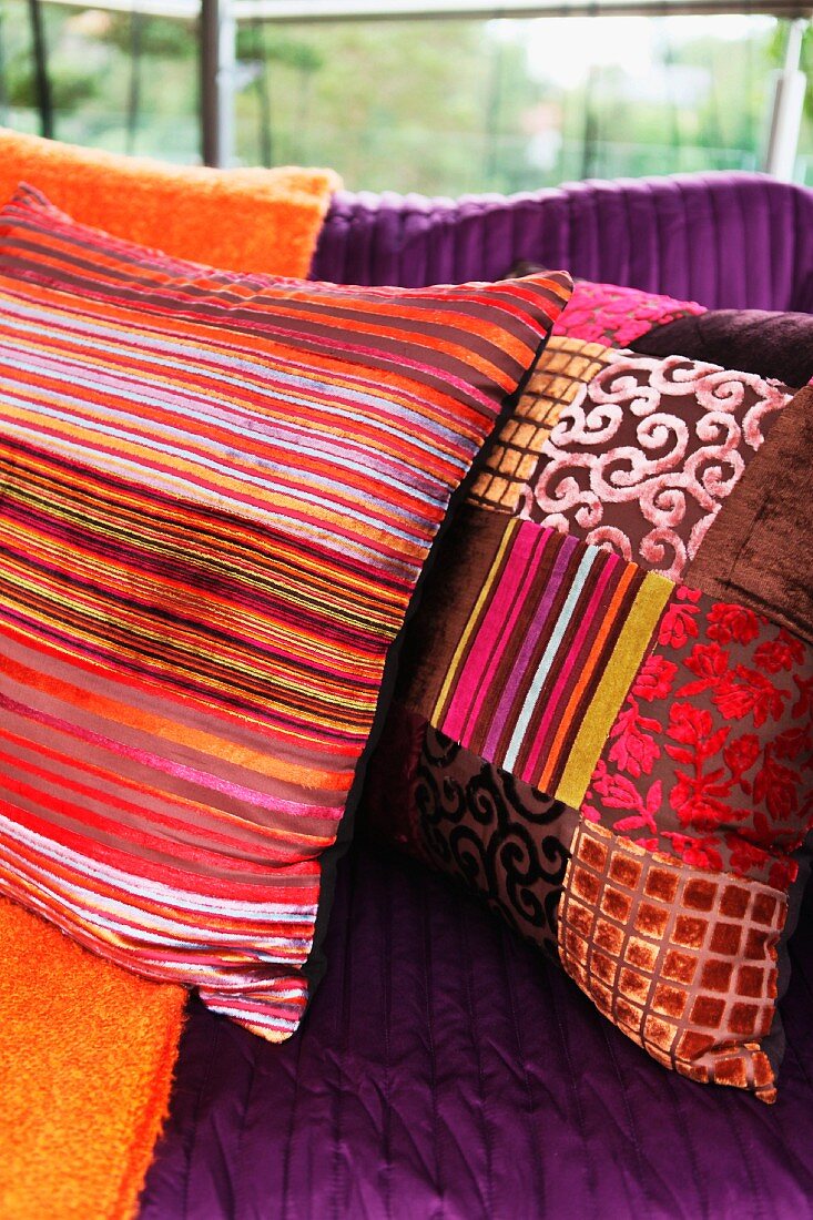 Farbige Kissen in verschiedenen Rottönen mit Streifen- und Patchwork Muster mit orientalischem Flair auf Couch