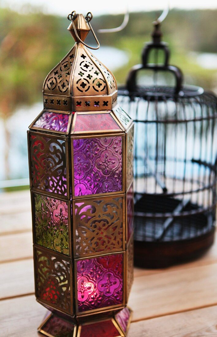 Laterne aus bronzefarbenem Metall und farbigen Glasscheiben in orientalischem Stil auf Holzterrasse