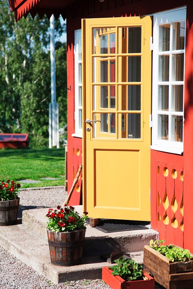 Halboffene Eingangstür in der verzierten, rot-gelb gestrichenen Fassade eines schwedischen Holzhauses