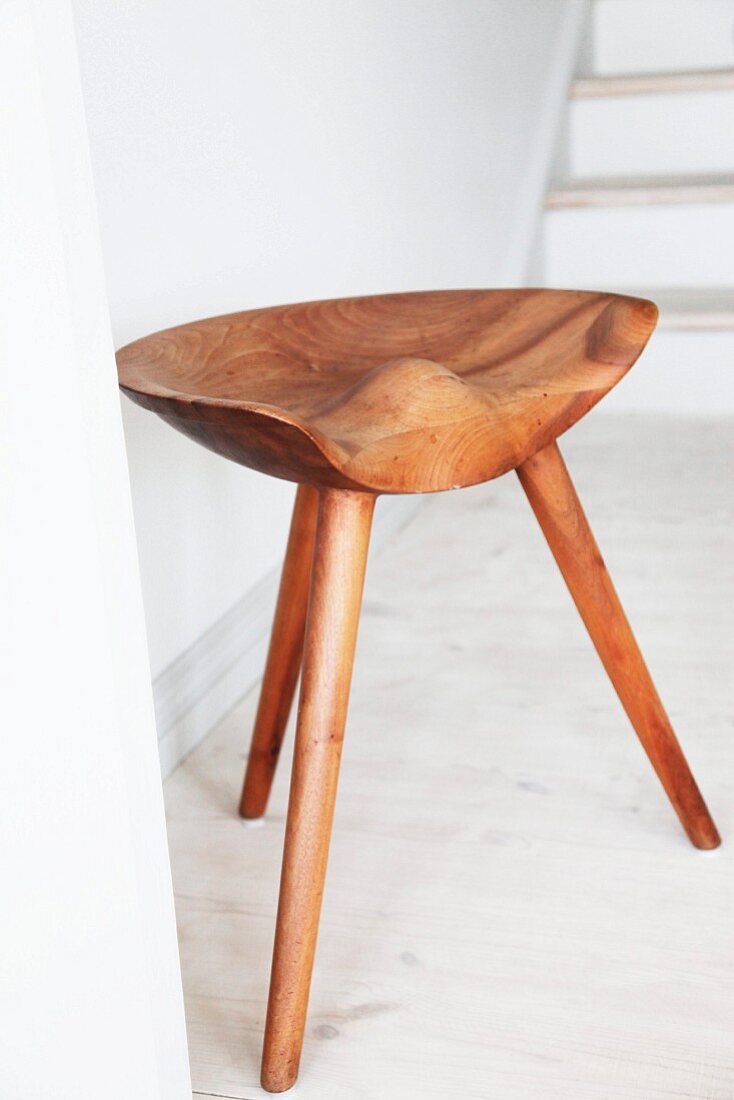 Three-legged wooden stool with ergonomic seat