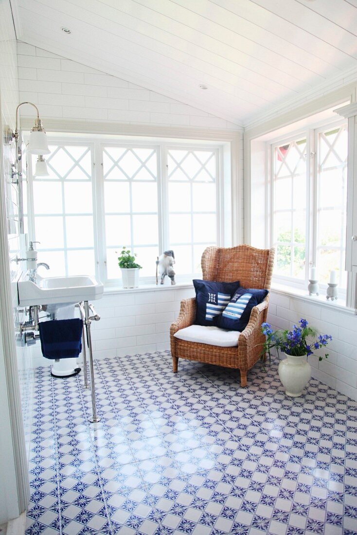 Sink and wicker armchair in conservatory-style extension with blue and white floor tiles and maritime scatter cushions