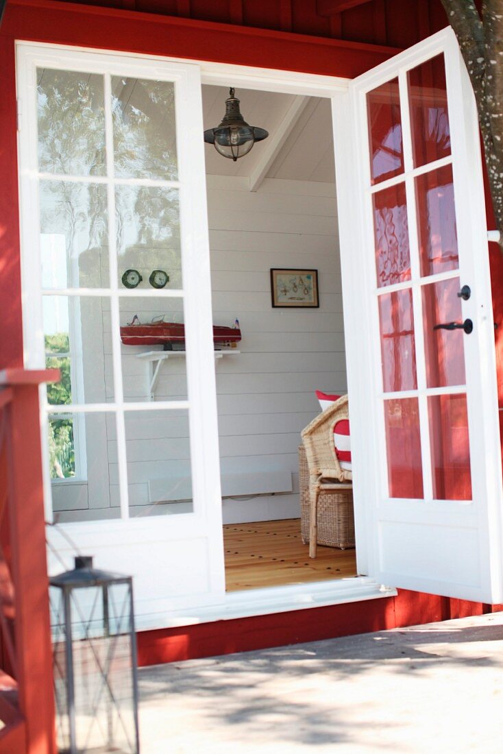 Blick von aussen durch die Fenstertür eines roten Holzhauses in Wohnraum