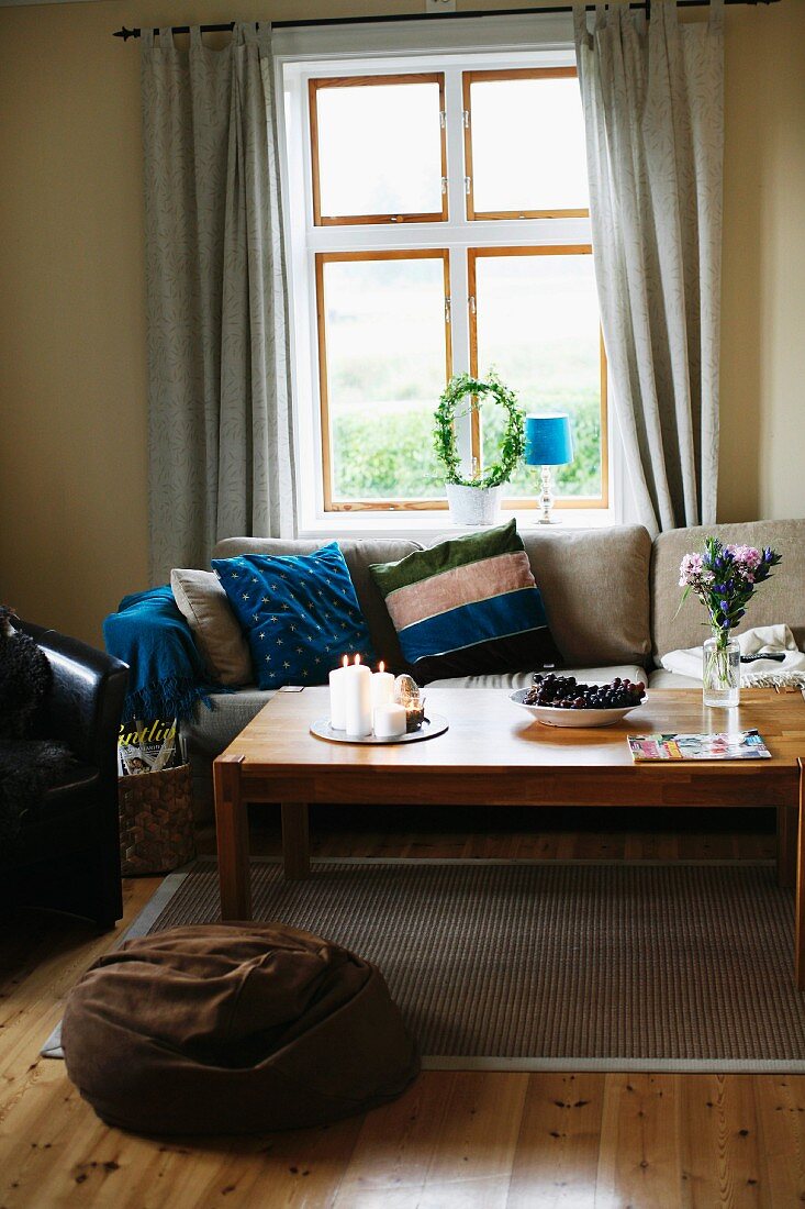 Holz Couchtisch und Sofa mit gestreiften Kissen vor Fenster, im Vordergrund braunes Sitzkissen, in ländlichem Ambiente
