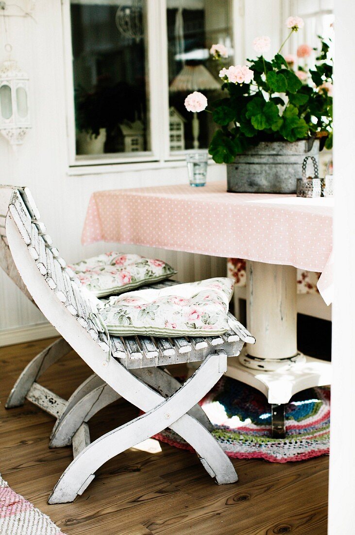 Weiß lackierte Holzstühle vor Tisch mit Blumentopf in Loggia