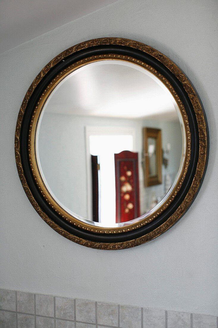 Round mirror with gilt frame on white wall