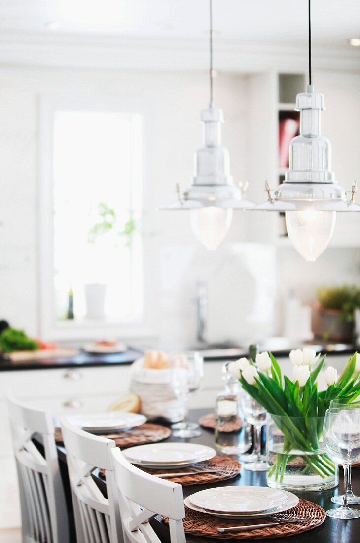 Retro, maritime pendant lamps and vase of tulips on festively set table in white, Scandinavian kitchen