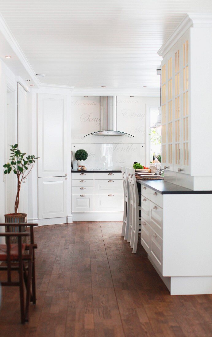 Open-plan, white, country-house kitchen with ample storage space and dark wooden floor