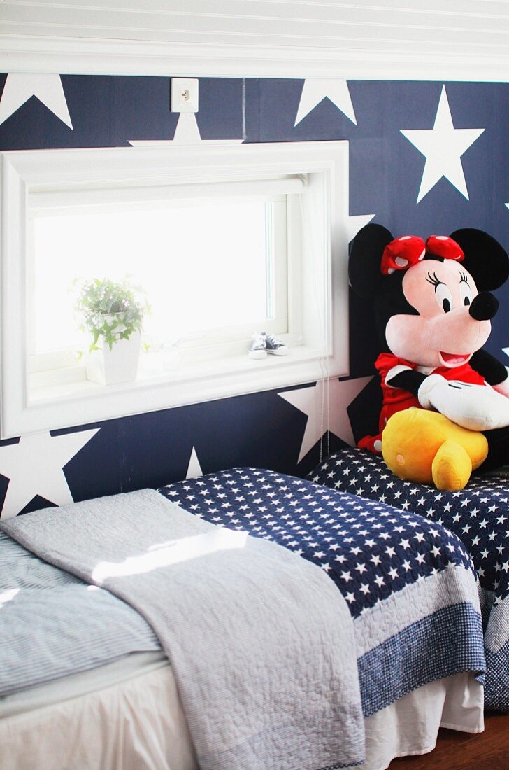 Twin beds and large Minnie Mouse soft toy in blue and white children's bedroom with patterns of stars on beds and wall