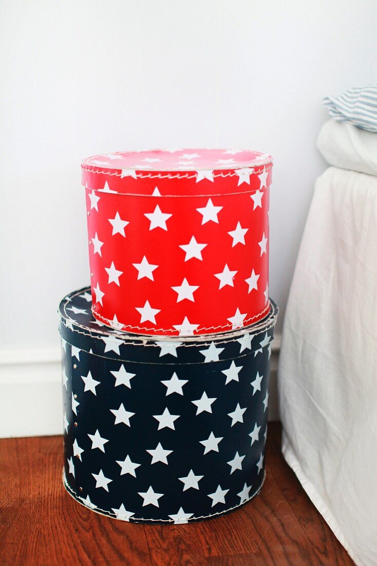 Red and black hat boxes with patterns of white stars on floor next to bed